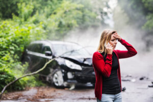 a young woman with smartphone by the damaged car after a car accident